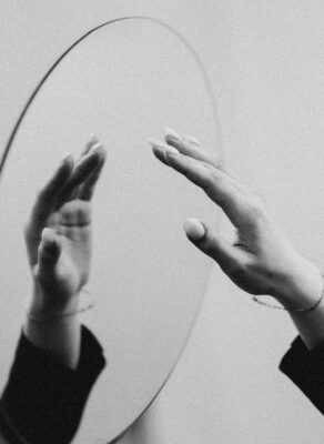 Zwart-witbeeld van handen die naar hun spiegelbeeld reiken