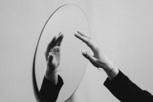 Zwart-witbeeld van handen die naar hun spiegelbeeld reiken