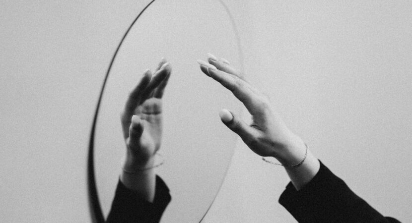 Zwart-witbeeld van handen die naar hun spiegelbeeld reiken