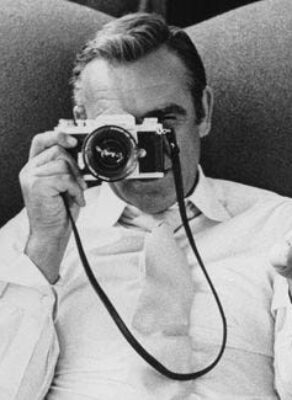Zwart-witfoto van een man die met een filmcamera naar de kijker wijst