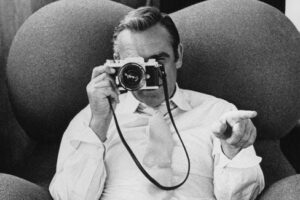 Zwart-witfoto van een man die met een filmcamera naar de kijker wijst