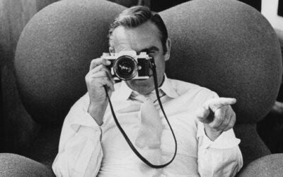 Zwart-witfoto van een man die met een filmcamera naar de kijker wijst