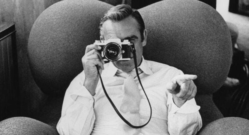 Zwart-witfoto van een man die met een filmcamera naar de kijker wijst