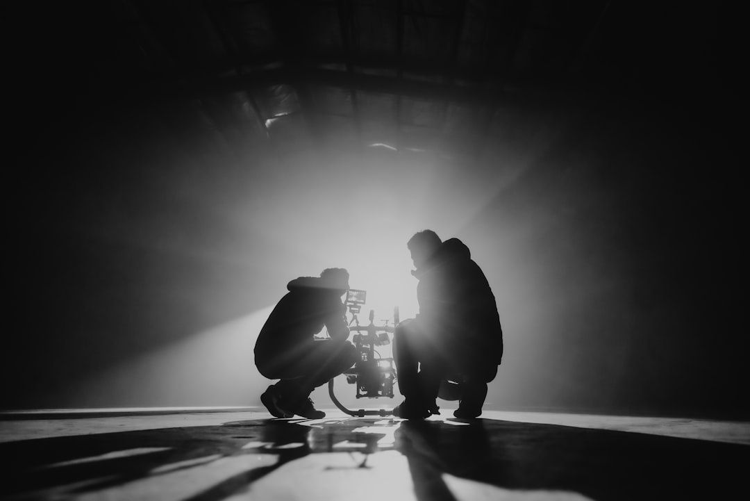 Twee silhouetten werken rond een filmcamera in een donkere studio